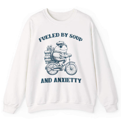 White sweatshirt with frog riding bicycle carrying soup cans and “Fueled by Soup and Anxiety” text – front view, by Shirtcasm